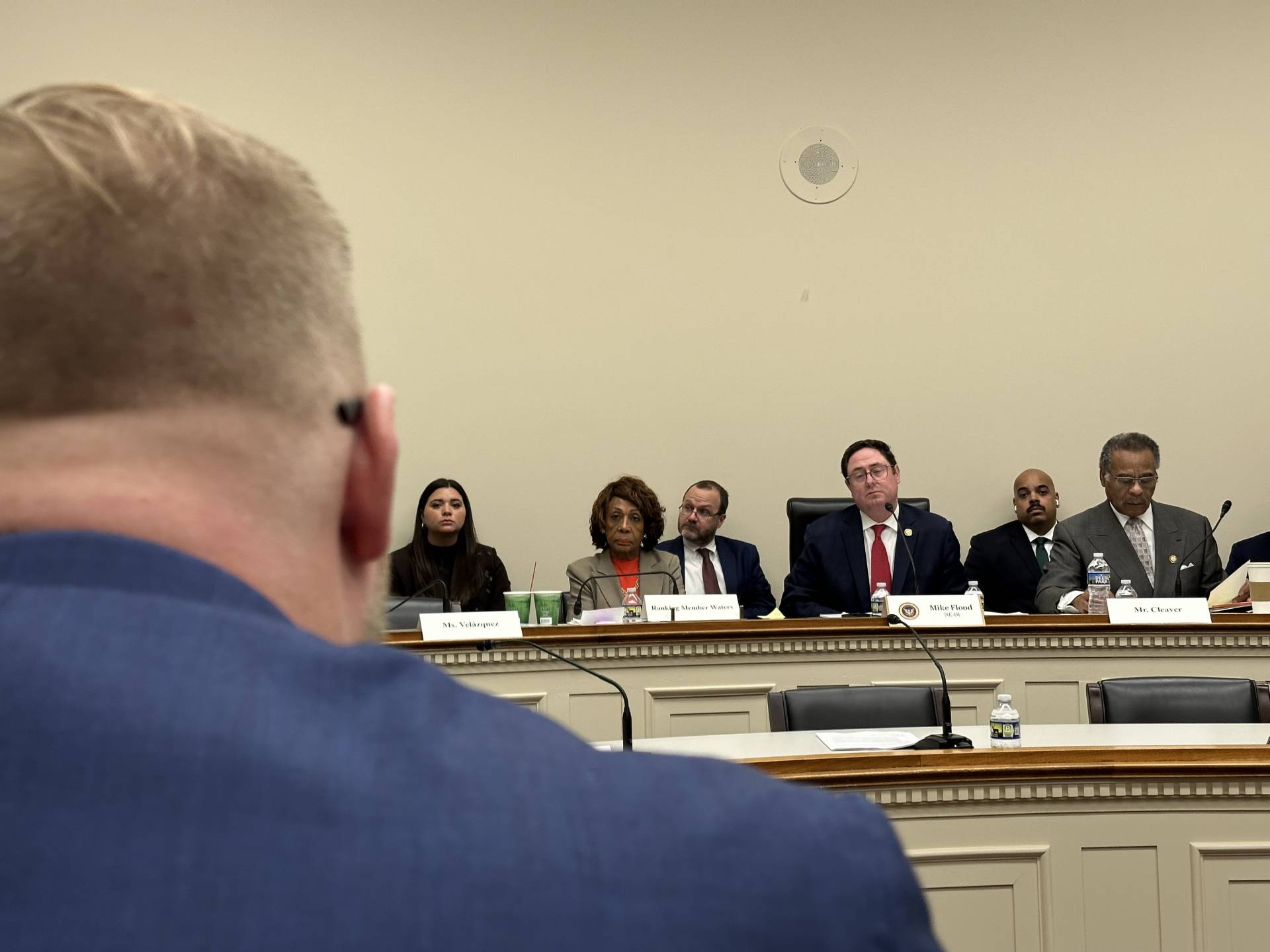 The back of a man's head looking towards a committee hearing.